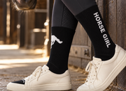 Black Iconic Horse Girl Boot Socks worn with cream sneakers in a stable